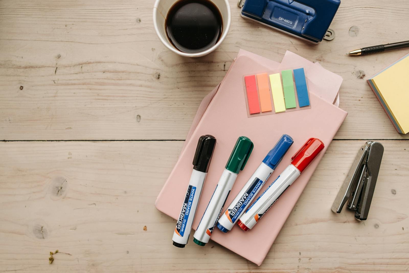 Top view of colorful office supplies, coffee, and stationery on a wooden desk.