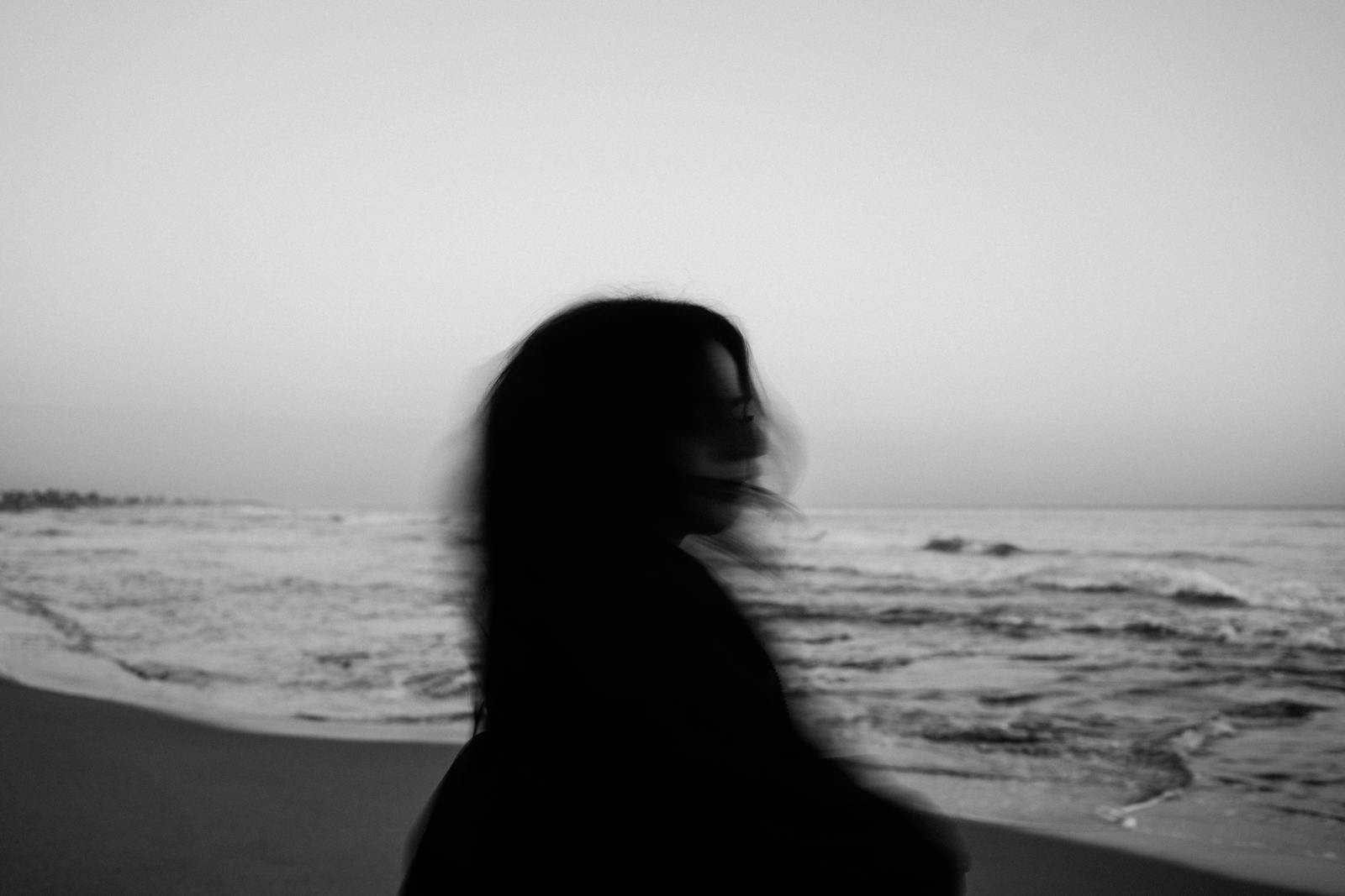 A silhouette of a woman with flowing hair on a peaceful beach, evoking solitude and tranquility.