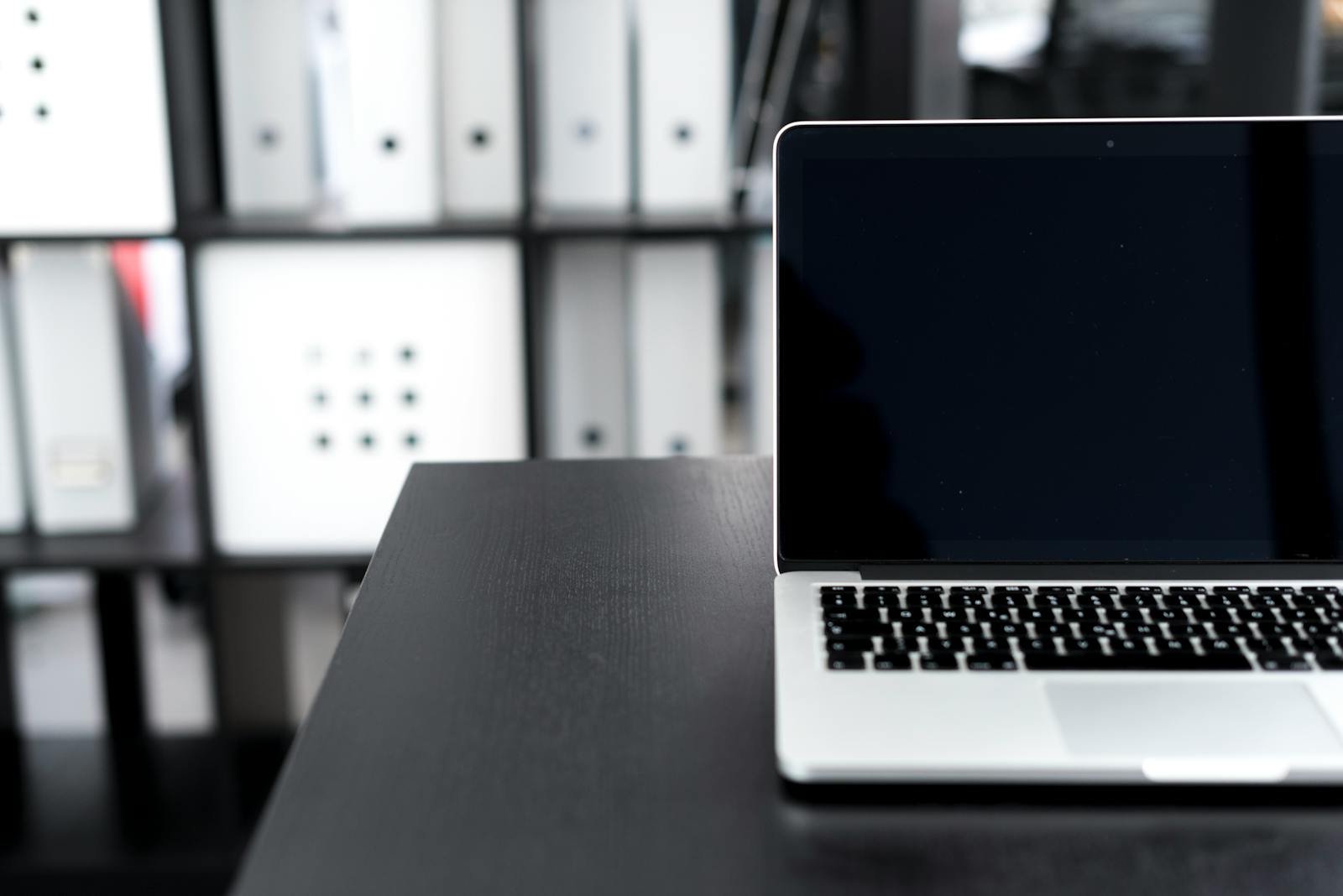 A sleek laptop on a desk in a modern office setting with organized shelves.