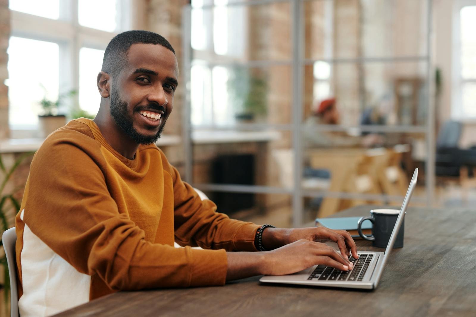 African American man typing on laptop in cozy modern office setting, smiling and focused.